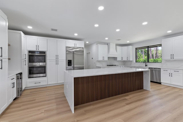 kitchen with appliances with stainless steel finishes, custom exhaust hood, beverage cooler, a center island, and light wood-style floors
