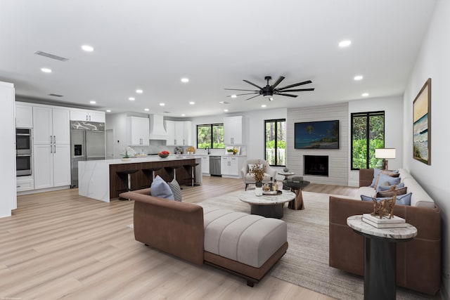 living area featuring recessed lighting, a large fireplace, light wood finished floors, and a ceiling fan