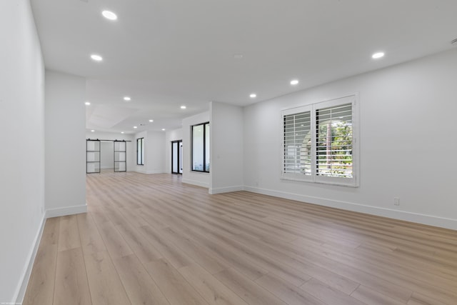 unfurnished living room with a barn door, light wood finished floors, baseboards, and recessed lighting