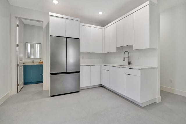 kitchen featuring freestanding refrigerator, baseboards, light countertops, white cabinetry, and a sink