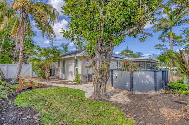 rear view of property featuring a sunroom, roof mounted solar panels, stucco siding, and fence