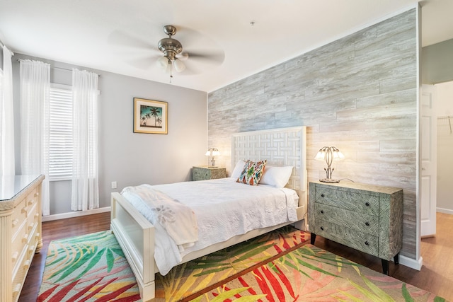 bedroom with wood finished floors, baseboards, an accent wall, and ceiling fan