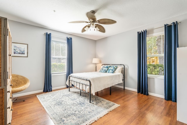 bedroom with multiple windows, light wood-type flooring, baseboards, and a textured ceiling
