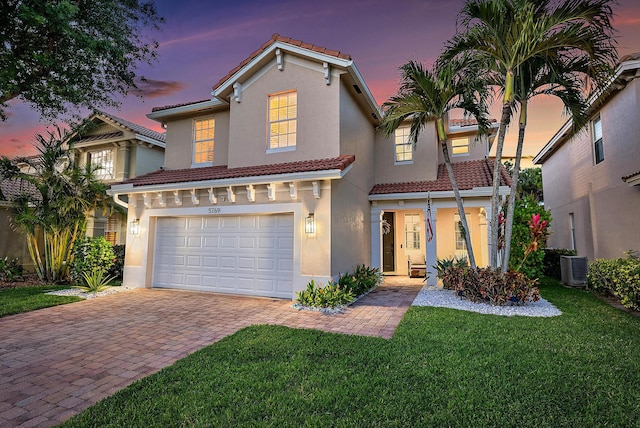 mediterranean / spanish-style home with a tile roof, a garage, decorative driveway, a front lawn, and stucco siding