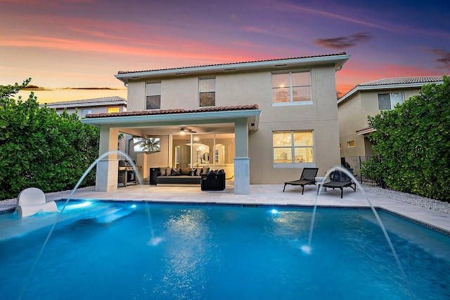 back of property at dusk featuring ceiling fan, outdoor lounge area, stucco siding, and an outdoor pool