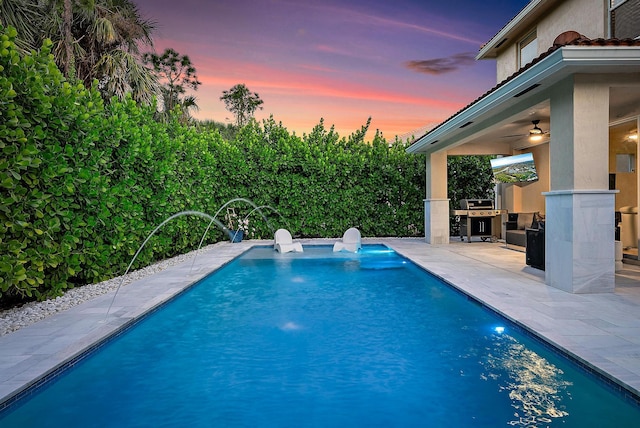 view of swimming pool featuring area for grilling, a ceiling fan, a patio area, a fenced in pool, and an outdoor kitchen