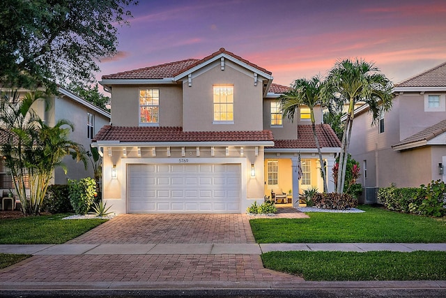 mediterranean / spanish home with an attached garage, decorative driveway, a front lawn, and a tile roof