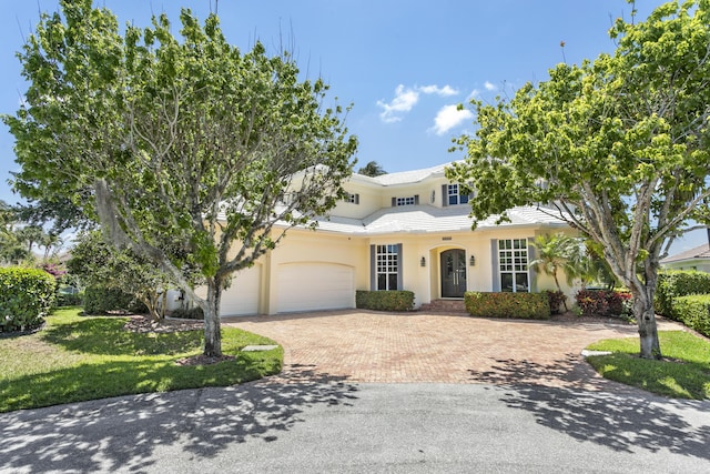 view of front of house with decorative driveway, stucco siding, an attached garage, and a front lawn