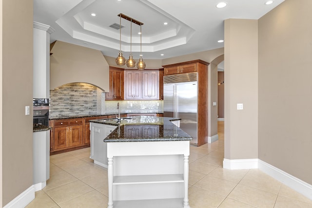 kitchen featuring arched walkways, built in refrigerator, a kitchen island with sink, custom range hood, and light tile patterned floors