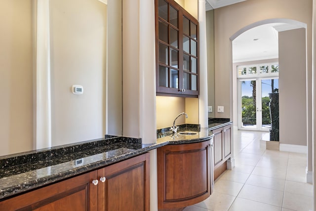 bar with arched walkways, a sink, ornamental molding, light tile patterned floors, and baseboards