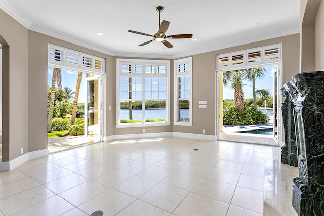 unfurnished living room with arched walkways, a ceiling fan, crown molding, baseboards, and tile patterned floors