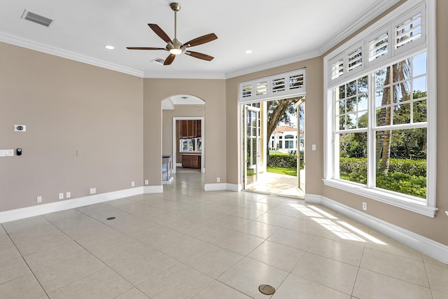 unfurnished room featuring a ceiling fan, arched walkways, light tile patterned floors, crown molding, and baseboards
