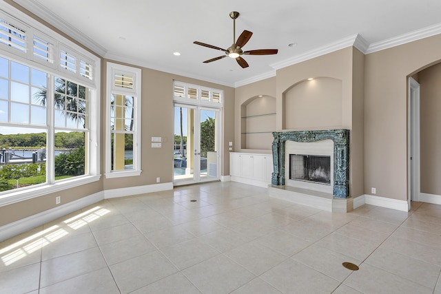 unfurnished living room featuring healthy amount of natural light, built in shelves, light tile patterned floors, baseboards, and ornamental molding