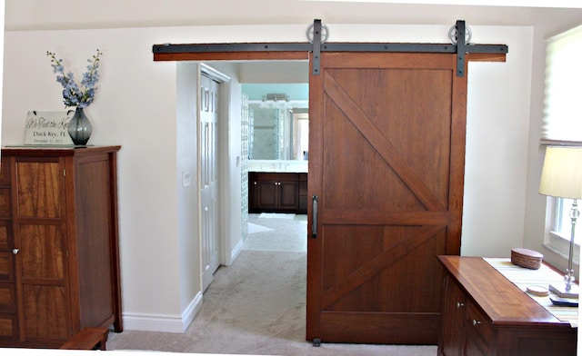 corridor with light colored carpet, baseboards, and a barn door