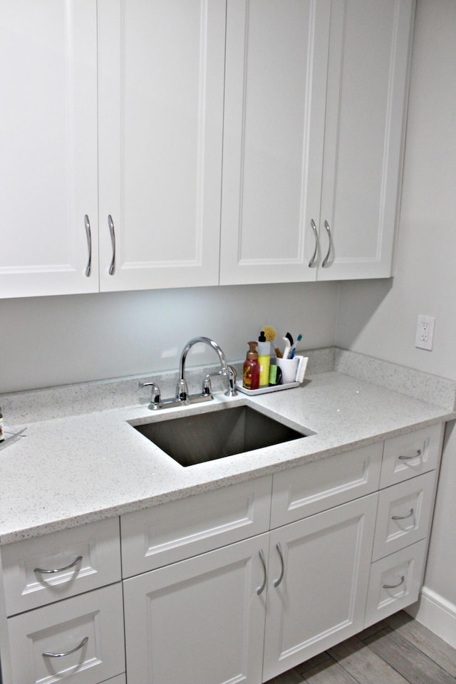 kitchen with a sink, white cabinetry, light stone countertops, and wood finished floors