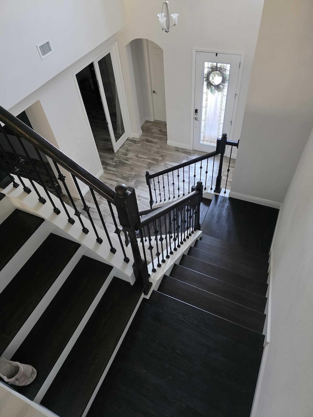 stairs featuring visible vents, an inviting chandelier, wood finished floors, baseboards, and arched walkways