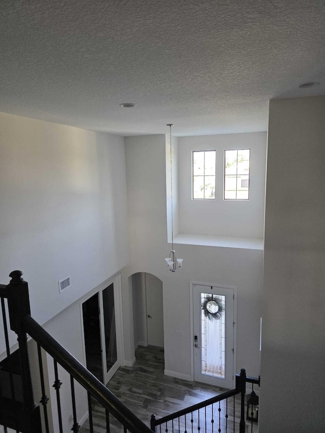 stairway featuring visible vents, wood finished floors, a high ceiling, a textured ceiling, and arched walkways