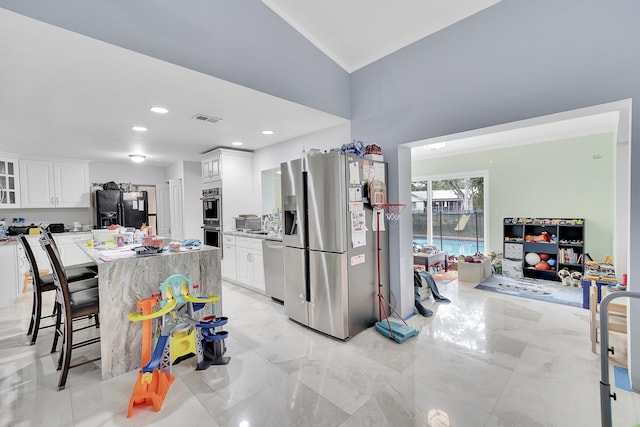 kitchen with a kitchen breakfast bar, visible vents, appliances with stainless steel finishes, glass insert cabinets, and white cabinetry