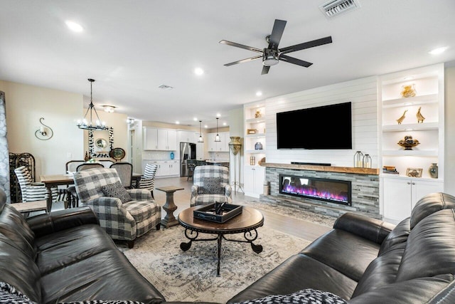 1220 Haywagon Trl, The Acreage, FL 33470 - living room featuring light wood finished floors, ceiling fan with notable chandelier, visible vents, a glass covered fireplace, and recessed lighting