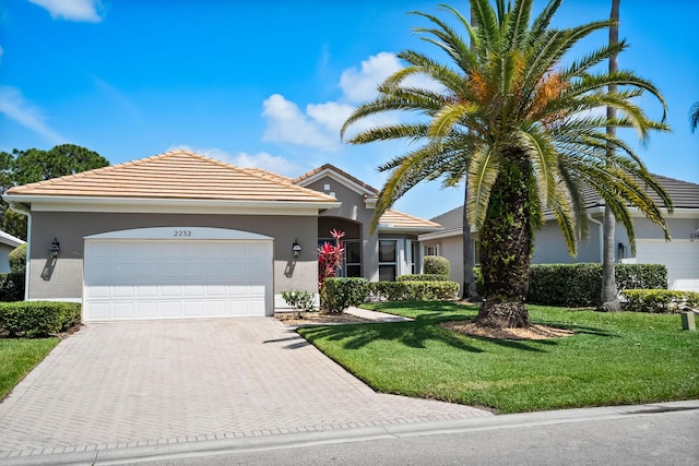 ranch-style house featuring driveway, a garage, stucco siding, a front lawn, and a tile roof