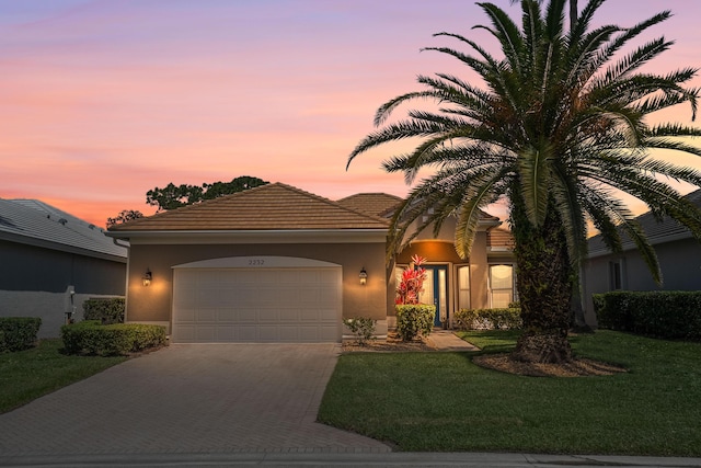view of front of home featuring driveway, an attached garage, stucco siding, a yard, and a tiled roof