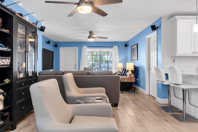 living room featuring a ceiling fan, baseboards, and light wood finished floors