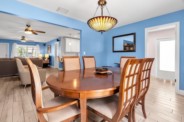 dining area featuring a ceiling fan, light wood-style floors, visible vents, and baseboards