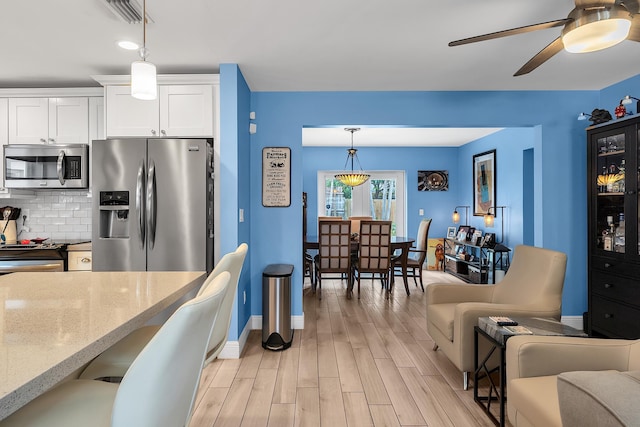kitchen featuring light wood finished floors, stainless steel appliances, white cabinets, light stone countertops, and ceiling fan