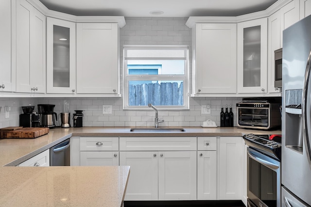 kitchen featuring a sink, a toaster, stainless steel appliances, white cabinets, and decorative backsplash