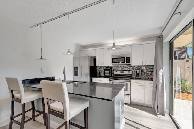 kitchen with stainless steel appliances, a textured ceiling, tasteful backsplash, a kitchen bar, and white cabinets