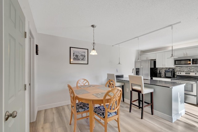 dining area featuring light wood-style flooring, a textured ceiling, and baseboards