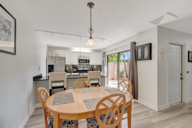 dining room with light wood-style floors, a textured ceiling, and baseboards