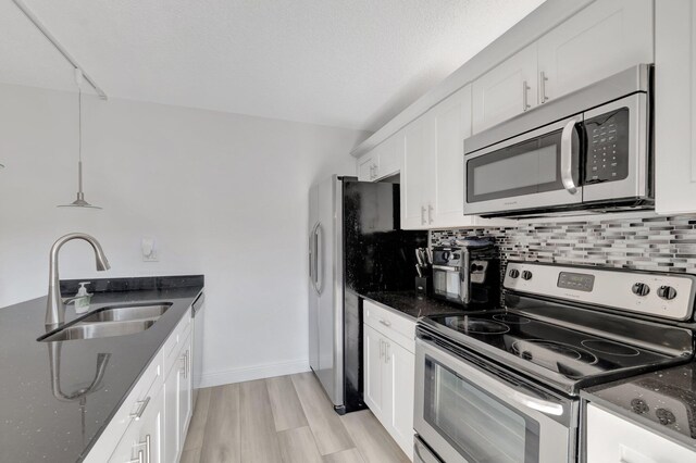 kitchen featuring stainless steel appliances, a sink, dark stone countertops, white cabinetry, and light wood-style floors