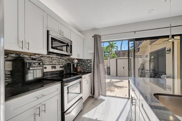 kitchen featuring appliances with stainless steel finishes, backsplash, dark stone counters, white cabinetry, and a textured ceiling