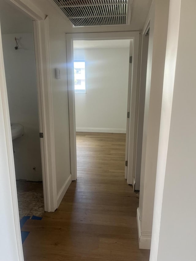 corridor with baseboards, wood finished floors, and visible vents
