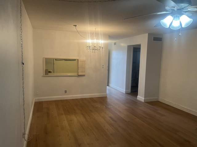 spare room with baseboards, ceiling fan with notable chandelier, wood finished floors, and visible vents