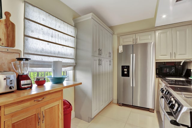 kitchen with butcher block counters, a toaster, a sink, appliances with stainless steel finishes, and light tile patterned floors