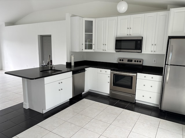 kitchen featuring a peninsula, dark tile patterned floors, a sink, appliances with stainless steel finishes, and vaulted ceiling