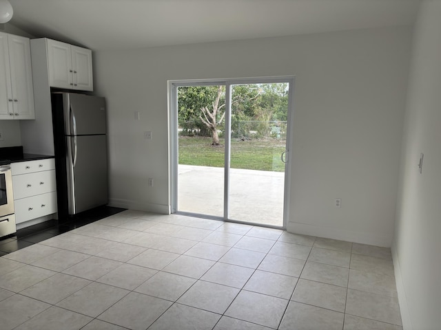 interior space with freestanding refrigerator, light tile patterned floors, white cabinets, baseboards, and dark countertops