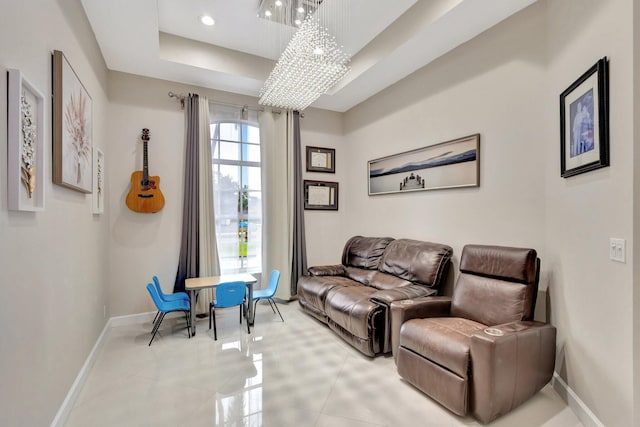 living area with a tray ceiling, an inviting chandelier, and baseboards