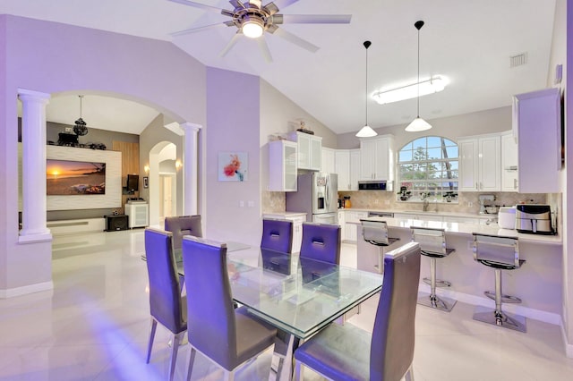 dining space featuring ornate columns, vaulted ceiling, arched walkways, a ceiling fan, and light tile patterned floors