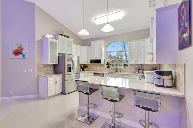 kitchen with a sink, a peninsula, decorative backsplash, a kitchen bar, and appliances with stainless steel finishes
