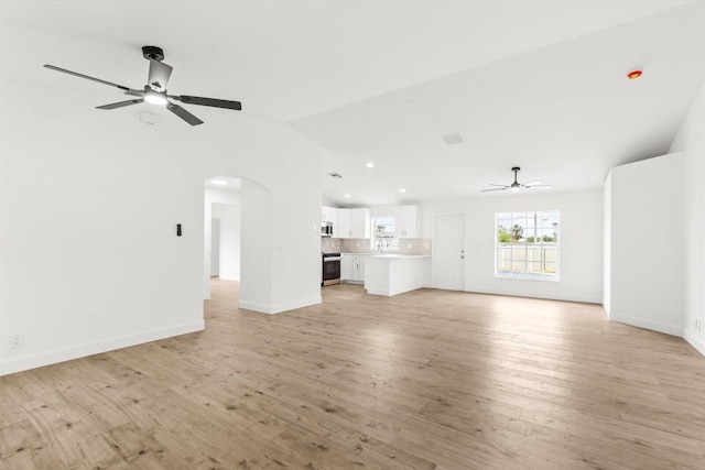 unfurnished living room with baseboards, arched walkways, ceiling fan, and vaulted ceiling