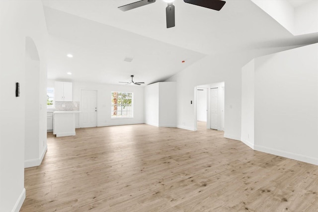 unfurnished living room with arched walkways, ceiling fan, vaulted ceiling, and light wood finished floors