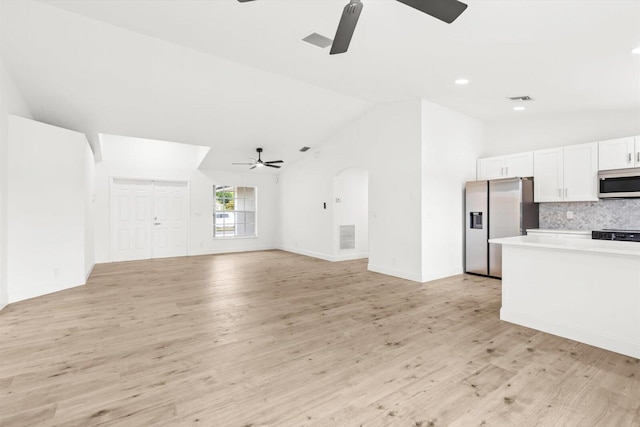 unfurnished living room with visible vents, arched walkways, a ceiling fan, light wood-style flooring, and vaulted ceiling