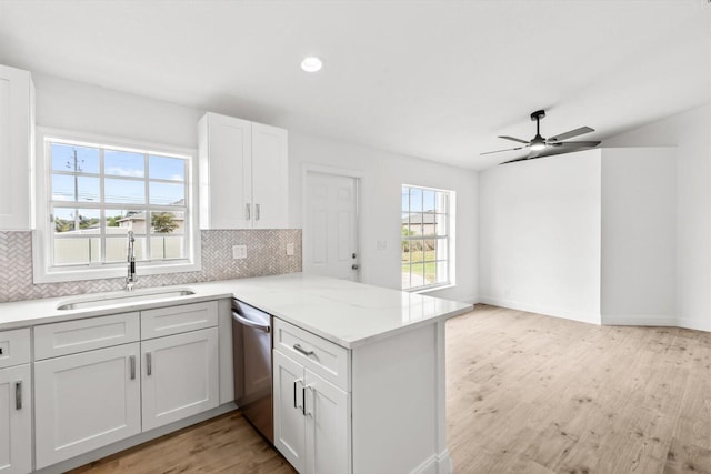 kitchen featuring a sink, dishwasher, light wood-style flooring, a peninsula, and tasteful backsplash