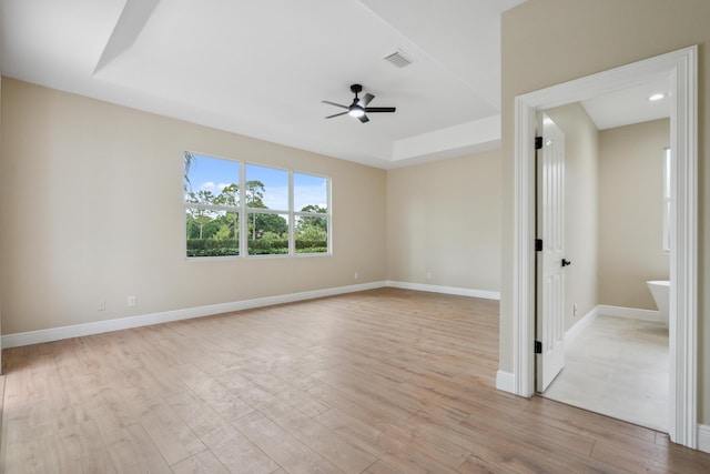 unfurnished room with ceiling fan, visible vents, a raised ceiling, baseboards, and light wood-style floors