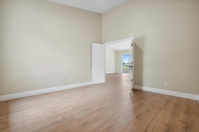 spare room with baseboards, light wood-style flooring, and high vaulted ceiling