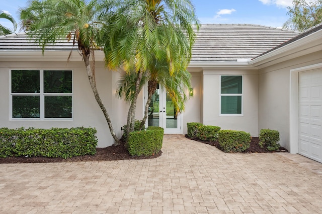entrance to property with a garage, driveway, french doors, and stucco siding
