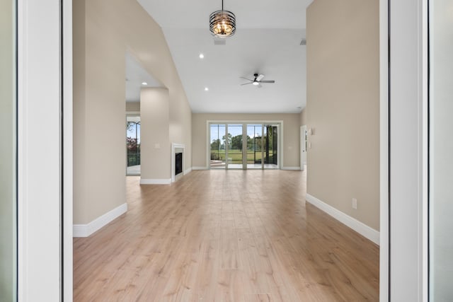 unfurnished living room with ceiling fan, a fireplace, baseboards, lofted ceiling, and light wood-type flooring